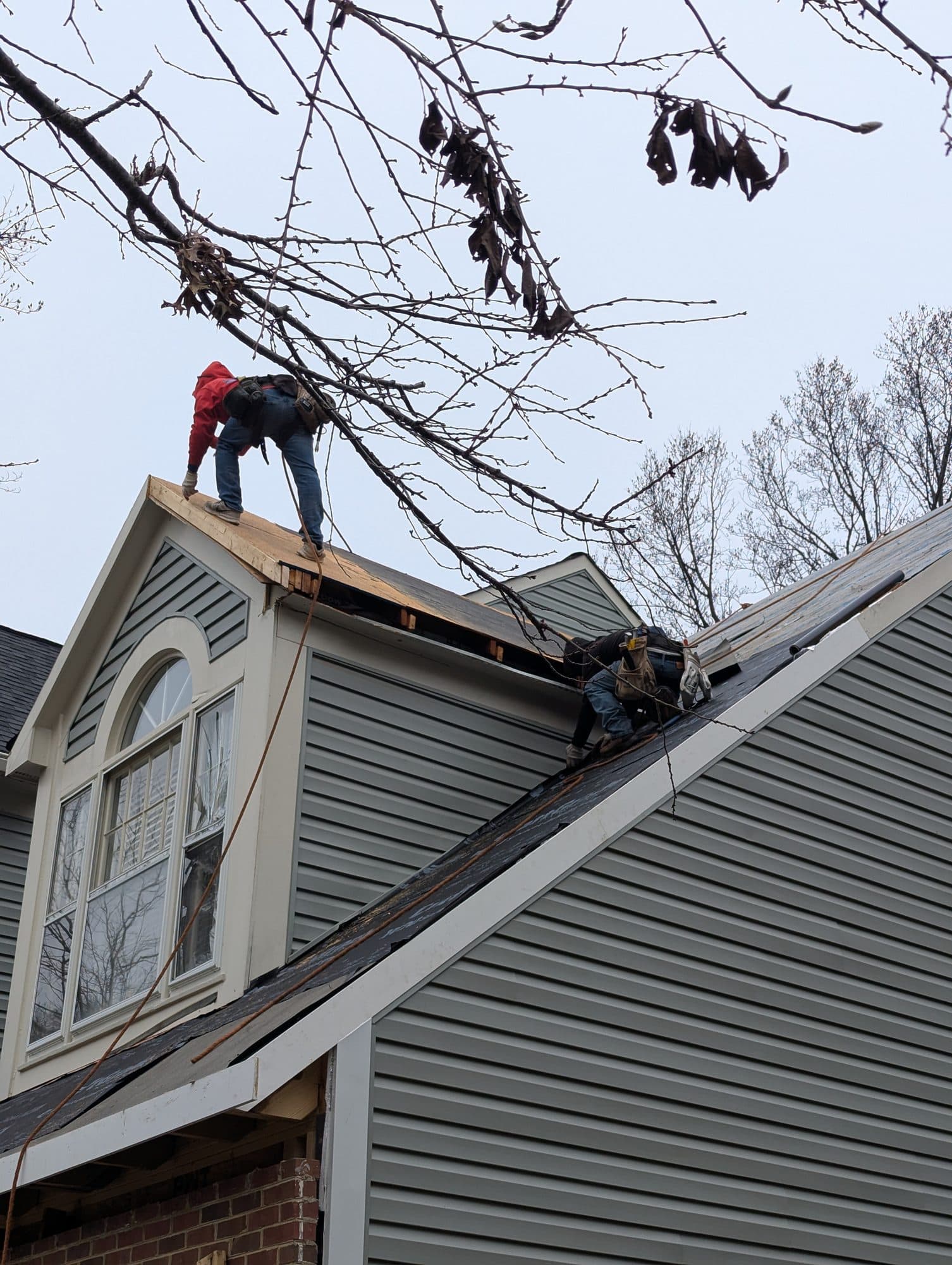 Roofing crew tearing off old shingles down to the decking on a dormer roof