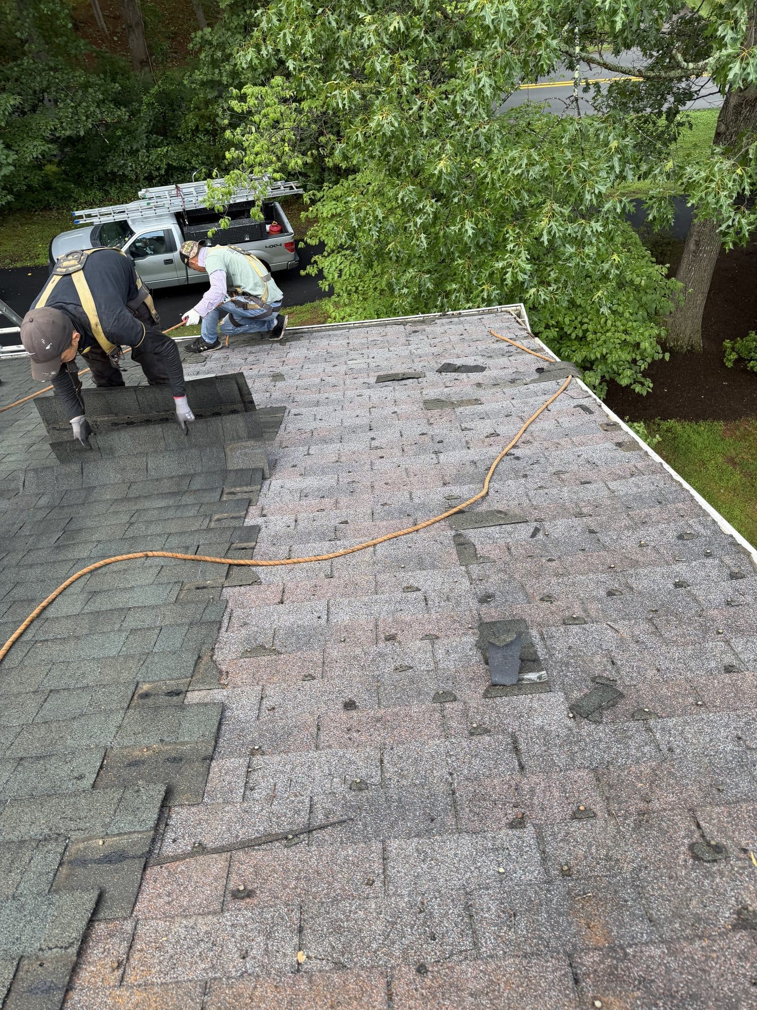 Roofing crew tearing off old shingles on a home's roof, with a work truck parked below
